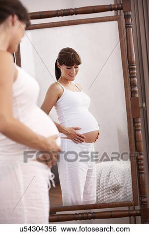 Stock Photograph - Pregnant woman looking in mirror. Fotosearch