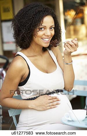 Stock Image - Pregnant woman sitting outside café. Fotosearch