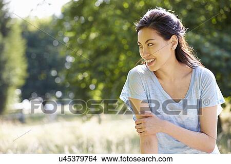 Picture - Pretty Asian Woman Sitting On Fence In Countryside. Fotosearch