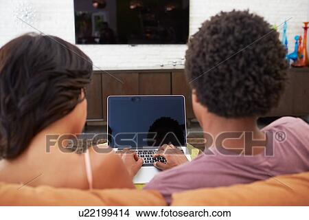 Picture - Rear View Of Couple Sitting On Sofa Using Laptop. Fotosearch