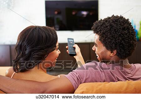 Rear View Of Couple Sitting On Sofa Watching TV Together View Large Photo Image Picture - Rear View Of Couple Sitting On Sofa Watching TV Together. Fotosearch