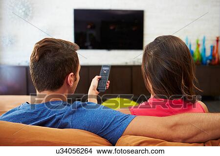 Picture - Rear View Of Couple Sitting On Sofa Watching TV Together. Fotosearch
