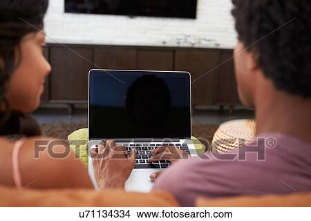 Picture - Rear View Of Couple Sitting On Sofa Using Laptop. Fotosearch