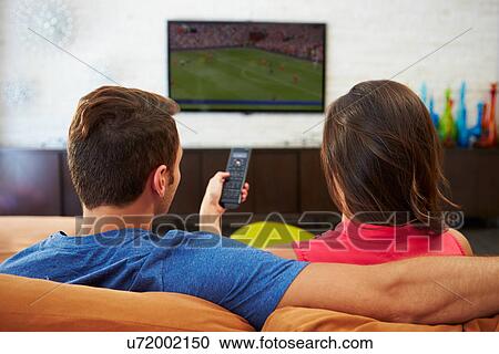 Stock Image - Rear View Of Couple Sitting On Sofa Watching TV Together. Fotosearch