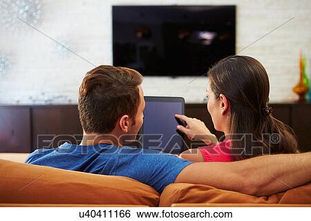 Stock Photograph - Rear View Of Couple Sitting On Sofa Using Digital Tablet. Fotosearch