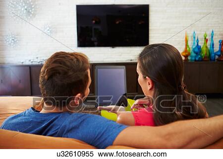 Stock Photography - Rear View Of Couple Sitting On Sofa Using Digital Tablet. Fotosearch