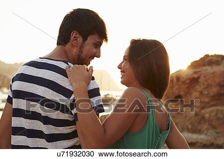 Stock Image - Rear View Of Couple Watching Sunset Over Harbour. Fotosearch