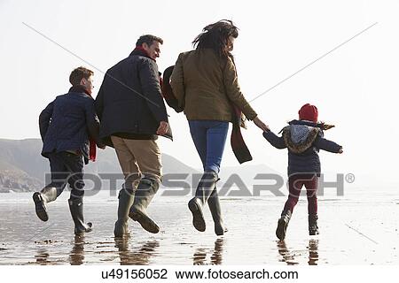Stock Image - Rear View Of Family Running Along Winter Beach. Fotosearch