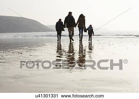Stock Image - Rear View Of Family Walking Along Winter Beach. Fotosearch