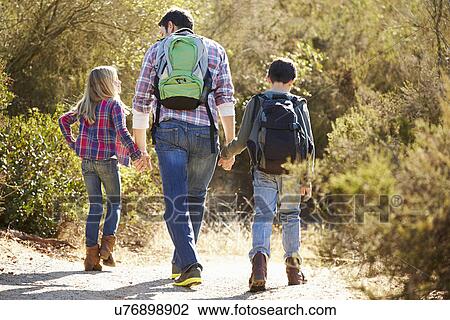 Stock Image - Rear View Of Father And Children Hiking In Countryside. Fotosearch