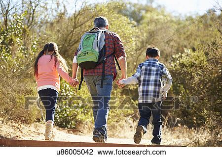 Stock Image - Rear View Of Father And Children Hiking In Countryside. Fotosearch