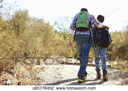 Stock Image - Rear View Of Father And Son Hiking In Countryside. Fotosearch