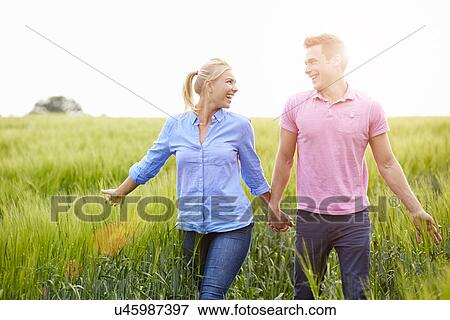 Stock Photo - Romantic Couple Walking In Field Holding Hands. Fotosearch