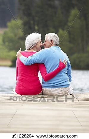 Picture - Romantic senior couple sitting on a jetty. Fotosearch