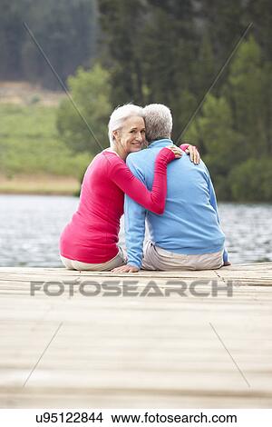 Picture - Romantic senior couple sitting on a jetty. Fotosearch
