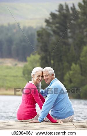 Stock Photo - Romantic senior couple sitting on a jetty. Fotosearch