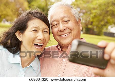 Stock Image - Senior Asian Couple Taking Selfie In Park Together. Fotosearch