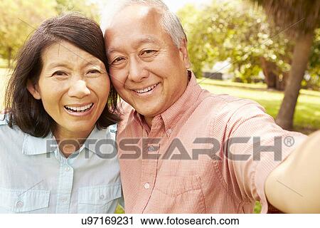 Stock Image - Senior Asian Couple Taking Selfie In Park Together. Fotosearch