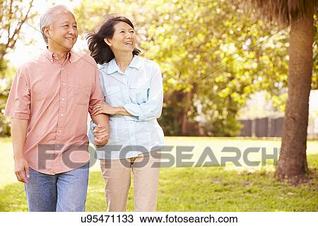 Stock Image - Senior Asian Couple Walking Through Park Together. Fotosearch