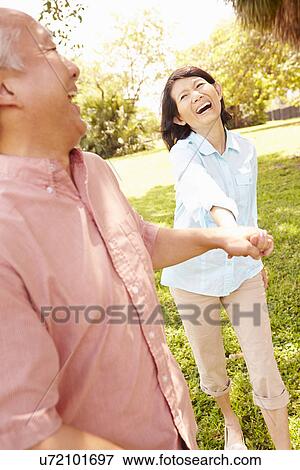 Stock Photo - Senior Asian Couple Walking Through Park Together. Fotosearch