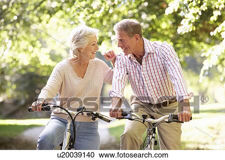 Stock Image - Senior couple cycling in park. Fotosearch
