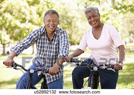 Stock Image - Senior couple cycling in park. Fotosearch