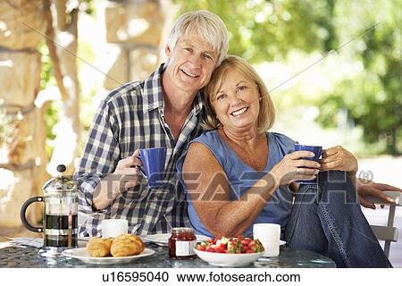 Stock Image - Senior couple eating breakfast outdoors. Fotosearch