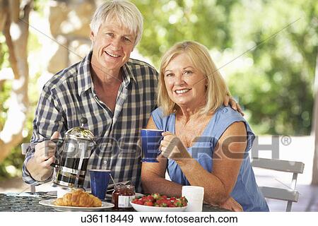 Stock Photo - Senior couple eating breakfast outdoors. Fotosearch