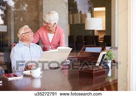 Stock Image - Senior Couple Looking At Photo Album Through Window. Fotosearch