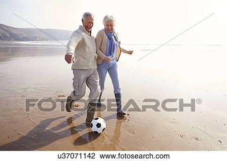 Stock Image - Senior Couple Playing Football On Winter Beach. Fotosearch
