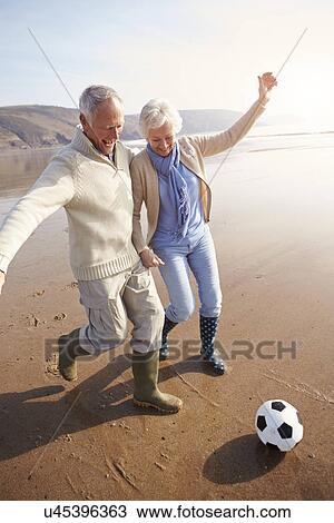 Stock Image - Senior Couple Playing Football On Winter Beach. Fotosearch