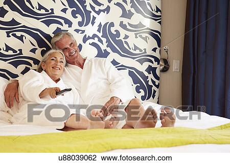 Stock Image - Senior Couple Relaxing In Hotel Room Watching Television. Fotosearch