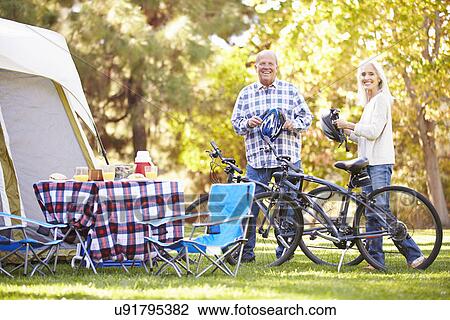 Stock Image - Senior Couple Riding Bikes On Camping Holiday In Countryside. Fotosearch