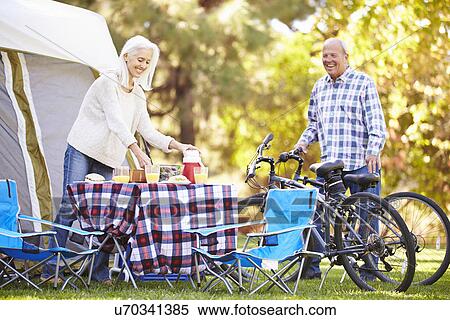 Stock Photography - Senior Couple Riding Bikes On Camping Holiday In Countryside. Fotosearch