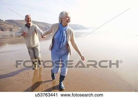 Stock Image - Senior Couple Running Along Winter Beach. Fotosearch