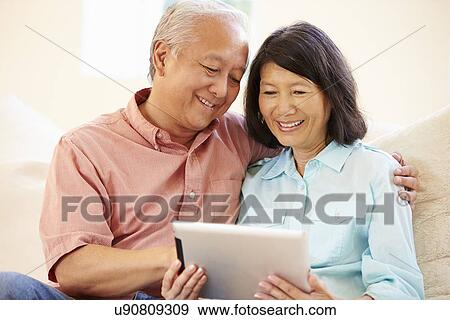 Senior Couple Sitting On Sofa Using Digital Tablet View Large Photo Image Stock Photo - Senior Couple Sitting On Sofa Using Digital Tablet. Fotosearch