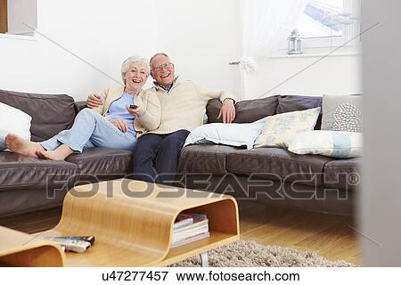 Stock Photo - Senior Couple Sitting On Sofa Watching TV. Fotosearch