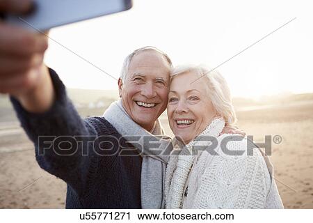 Stock Image - Senior Couple Standing On Beach Taking Selfie. Fotosearch