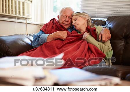 Stock Image - Senior Couple Trying To Keep Warm Under Blanket At Home. Fotosearch