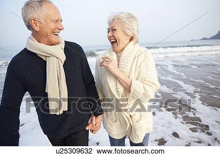 Stock Image - Senior Couple Walking Along Winter Beach. Fotosearch
