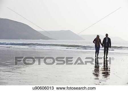 Stock Image - Senior Couple Walking Along Winter Beach. Fotosearch