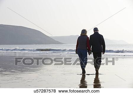 Stock Photo - Senior Couple Walking Along Winter Beach. Fotosearch