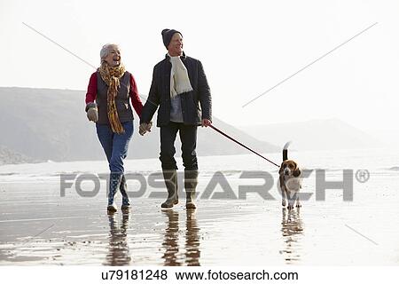 Stock Photo - Senior Couple Walking Along Winter Beach With Pet Dog. Fotosearch