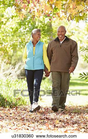 Stock Image - Senior Couple Walking Through Autumn Woodland. Fotosearch
