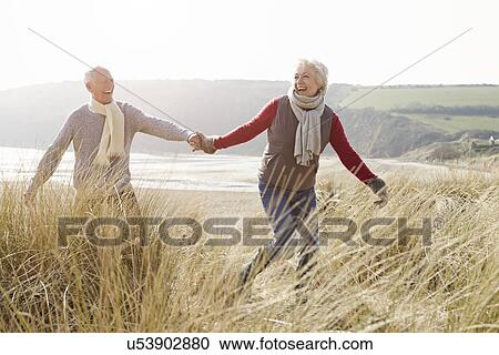 Senior Couple Walking Through Sand Dunes On Winter Beach View Large Photo Image Stock Image - Senior Couple Walking Through Sand Dunes On Winter Beach. Fotosearch
