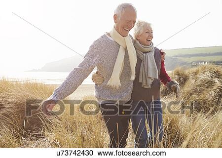 Senior Couple Walking Through Sand Dunes On Winter Beach View Large Photo Image Stock Image - Senior Couple Walking Through Sand Dunes On Winter Beach. Fotosearch