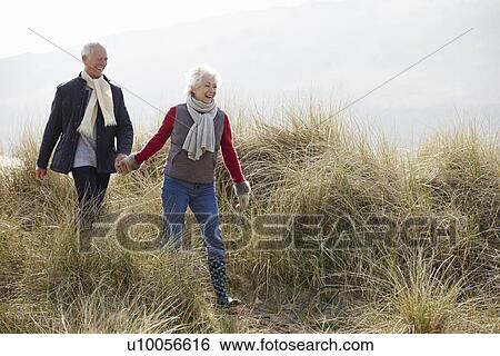 Senior Couple Walking Through Sand Dunes On Winter Beach View Large Photo Image Stock Photograph - Senior Couple Walking Through Sand Dunes On Winter Beach. Fotosearch
