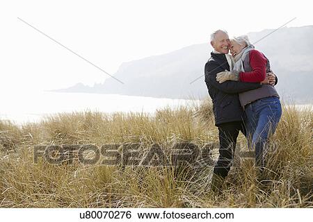 Senior Couple Walking Through Sand Dunes On Winter Beach View Large Photo Image Stock Photograph - Senior Couple Walking Through Sand Dunes On Winter Beach. Fotosearch
