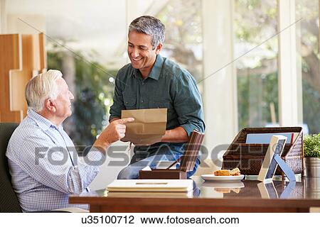 Stock Image - Senior Father Discussing Document With Adult Son. Fotosearch