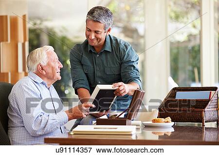 Stock Photo - Senior Father Looking At Photo In Frame With Adult Son. Fotosearch